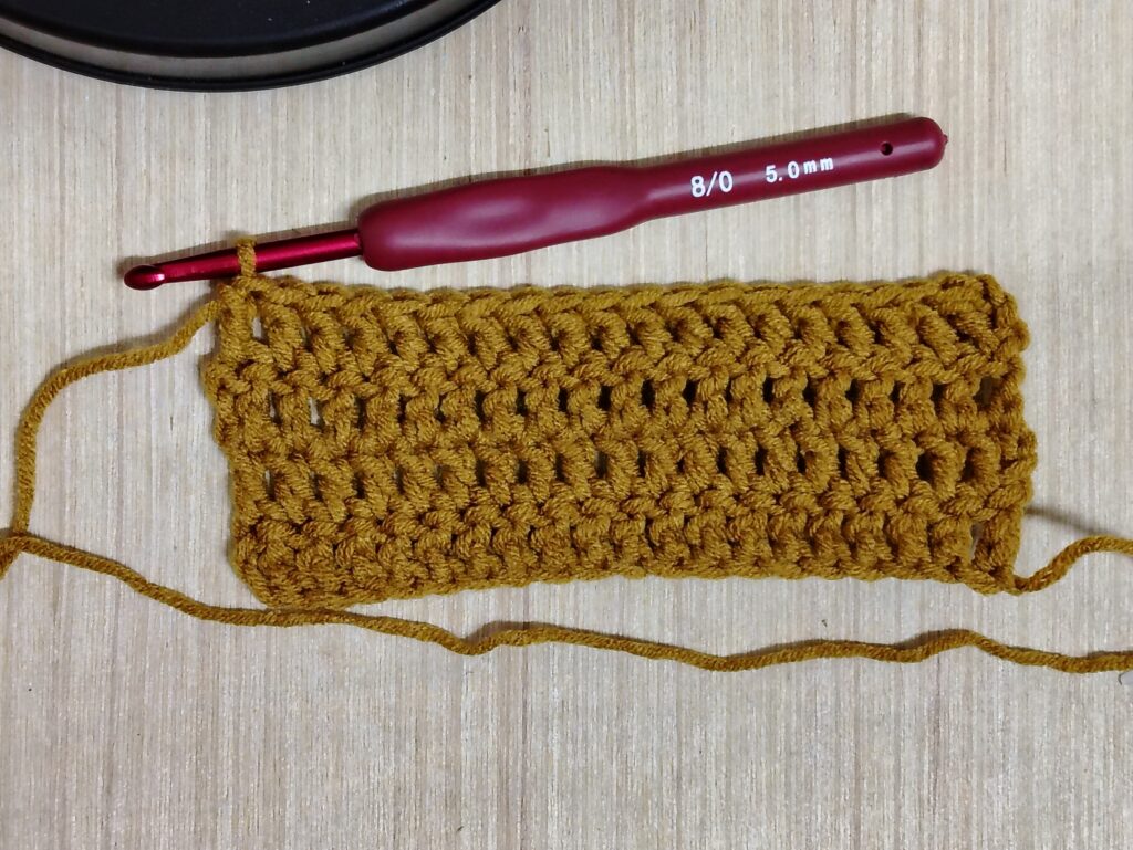 Mustard-colored double crochet swatch showing uneven, wonky edges before trying the stacked single crochet technique.